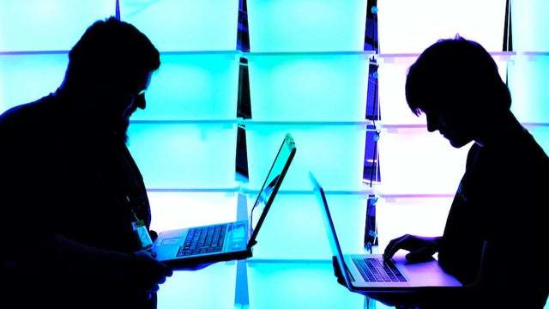 Mentor and apprentice on laptops, silhouetted against bright lights.